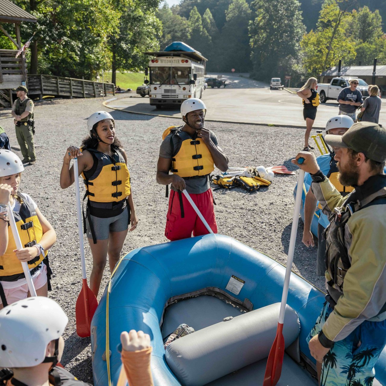 group of people wearing helmets and life vest listening to a ranger instructor on a raft