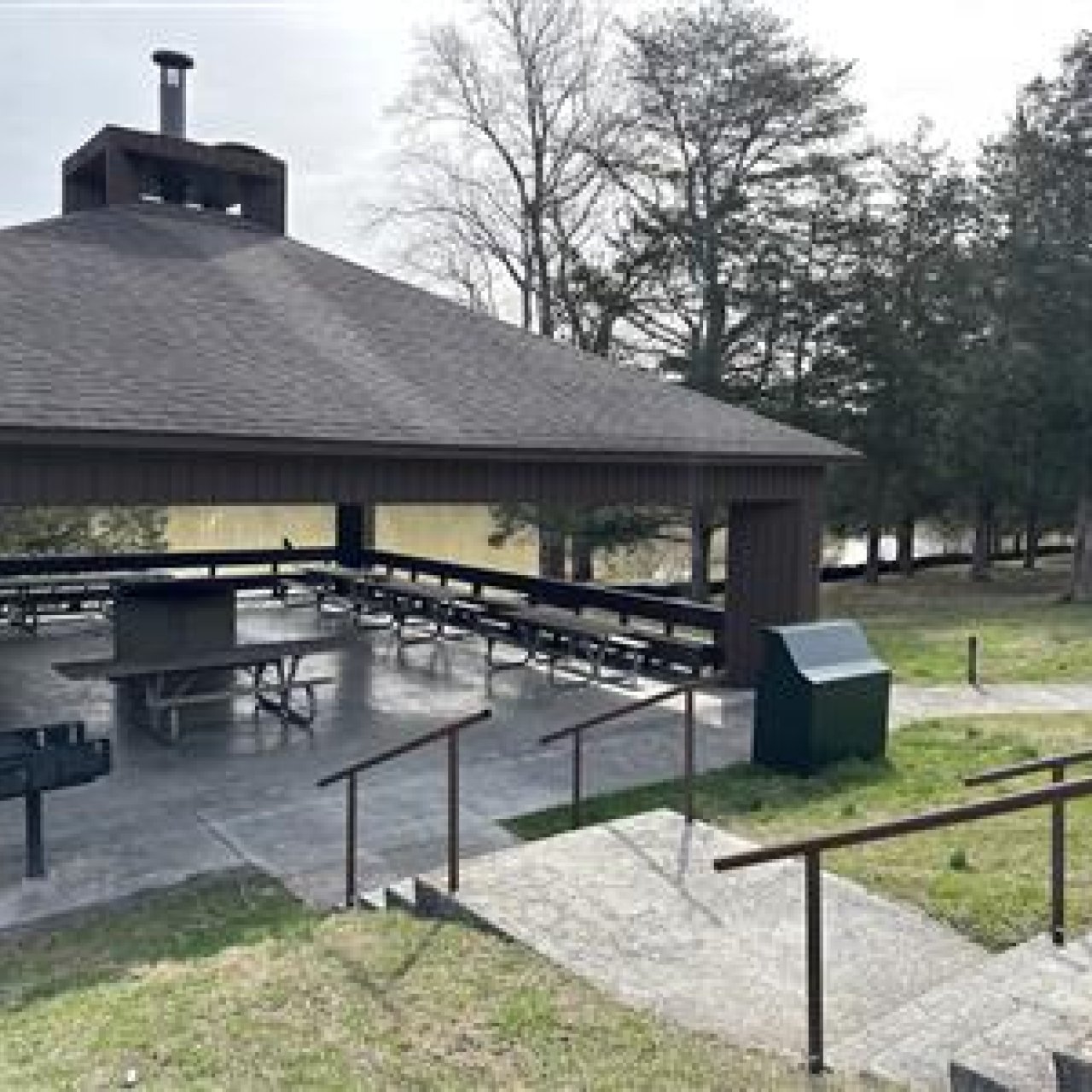 Outdoor pavilion with a large grill and picnic tables in a park.