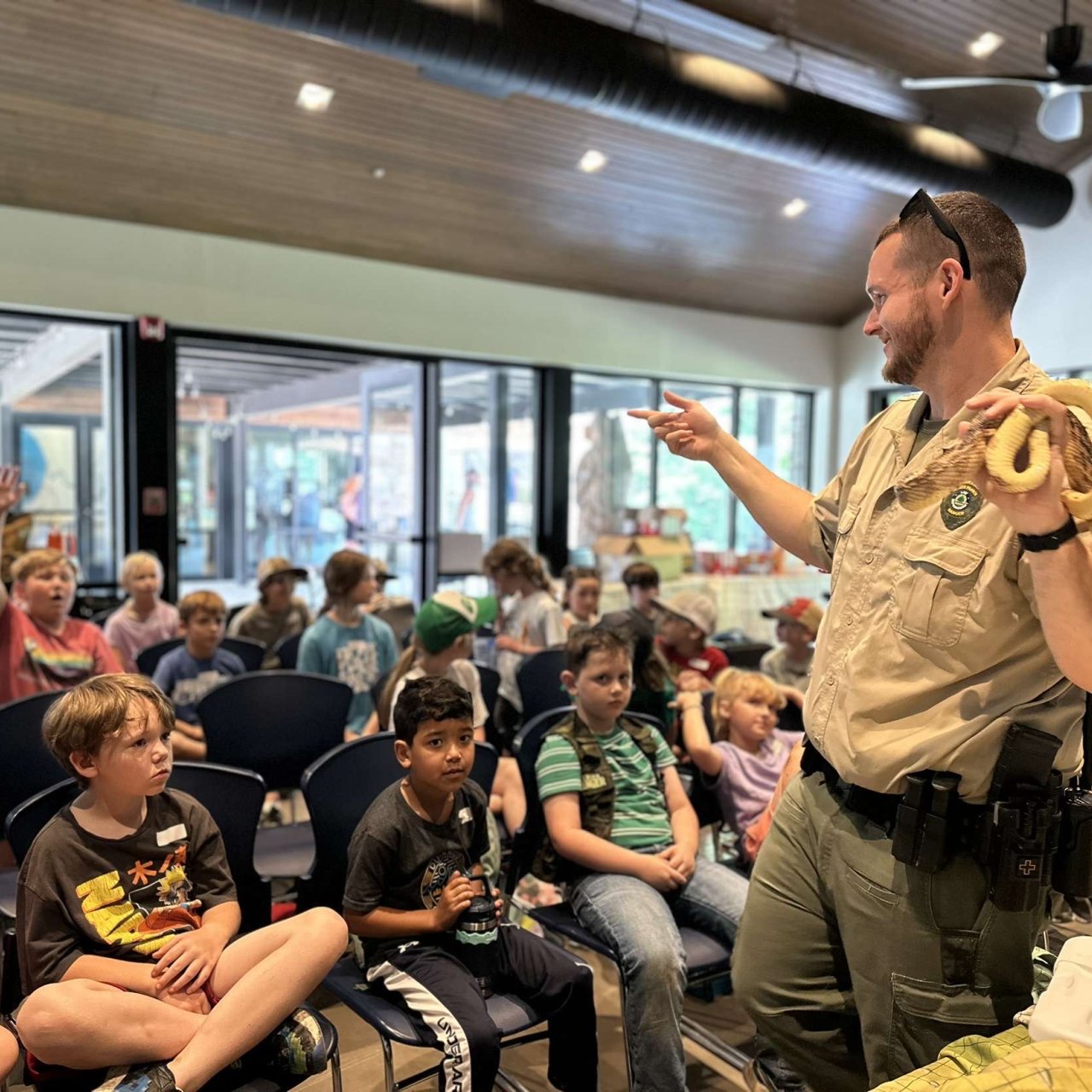 Ranger presenting a snake to a group of children in a classroom.