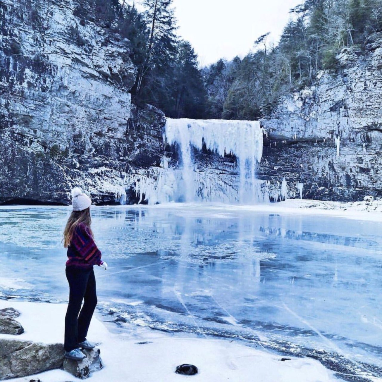 Woman in winter clothes admiring a frozen waterfall and icy river.