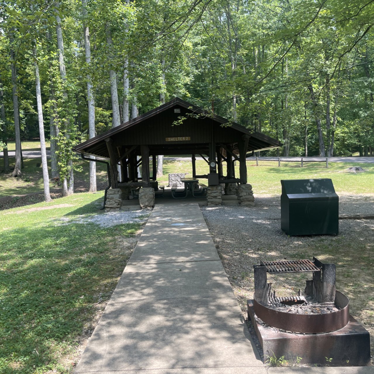 Path leading to a picnic pavilion in a sunny park with trees.