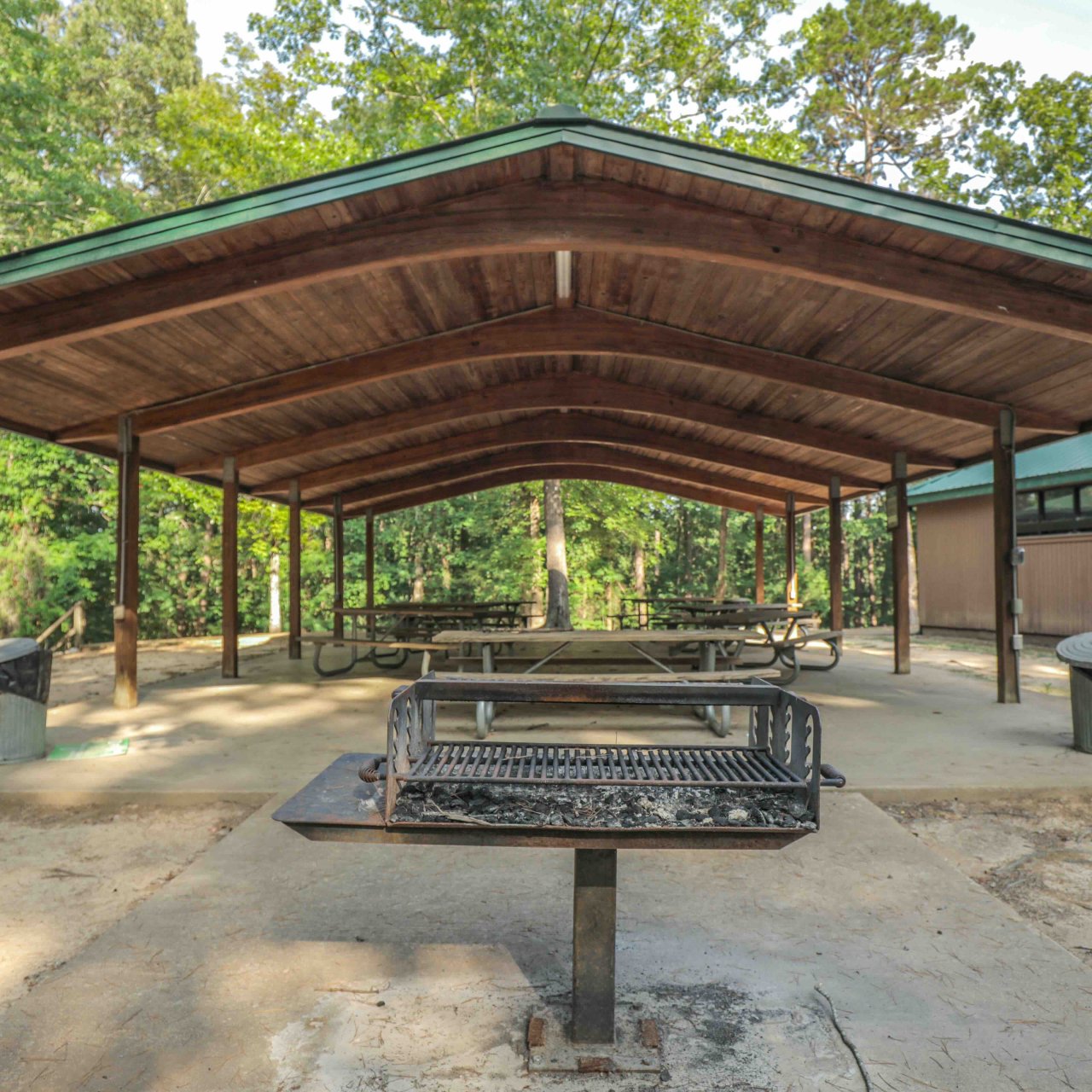 Large picnic shelter with grill and benches in a forest park.