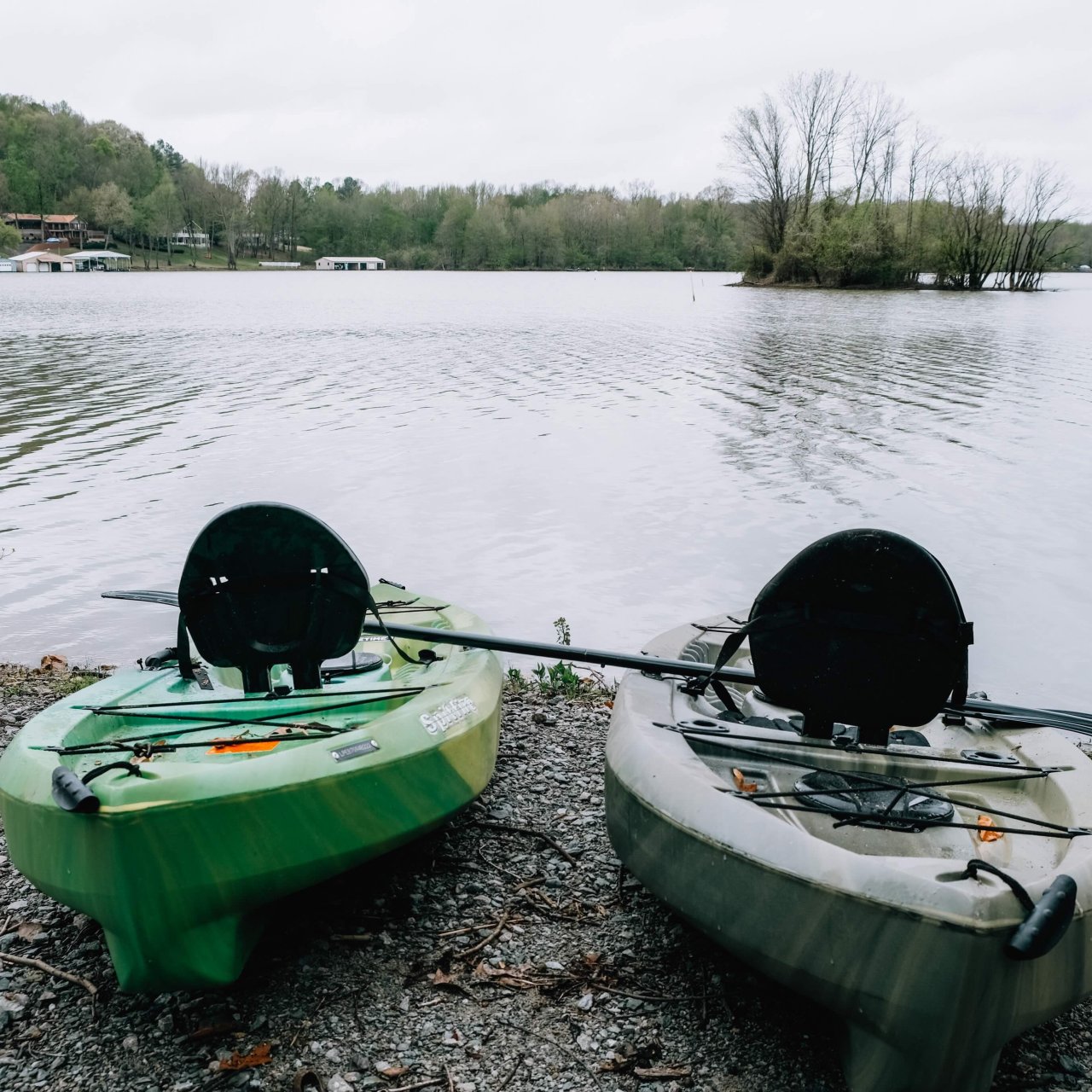 Two green kayaks with paddles beside a tranquil lake.