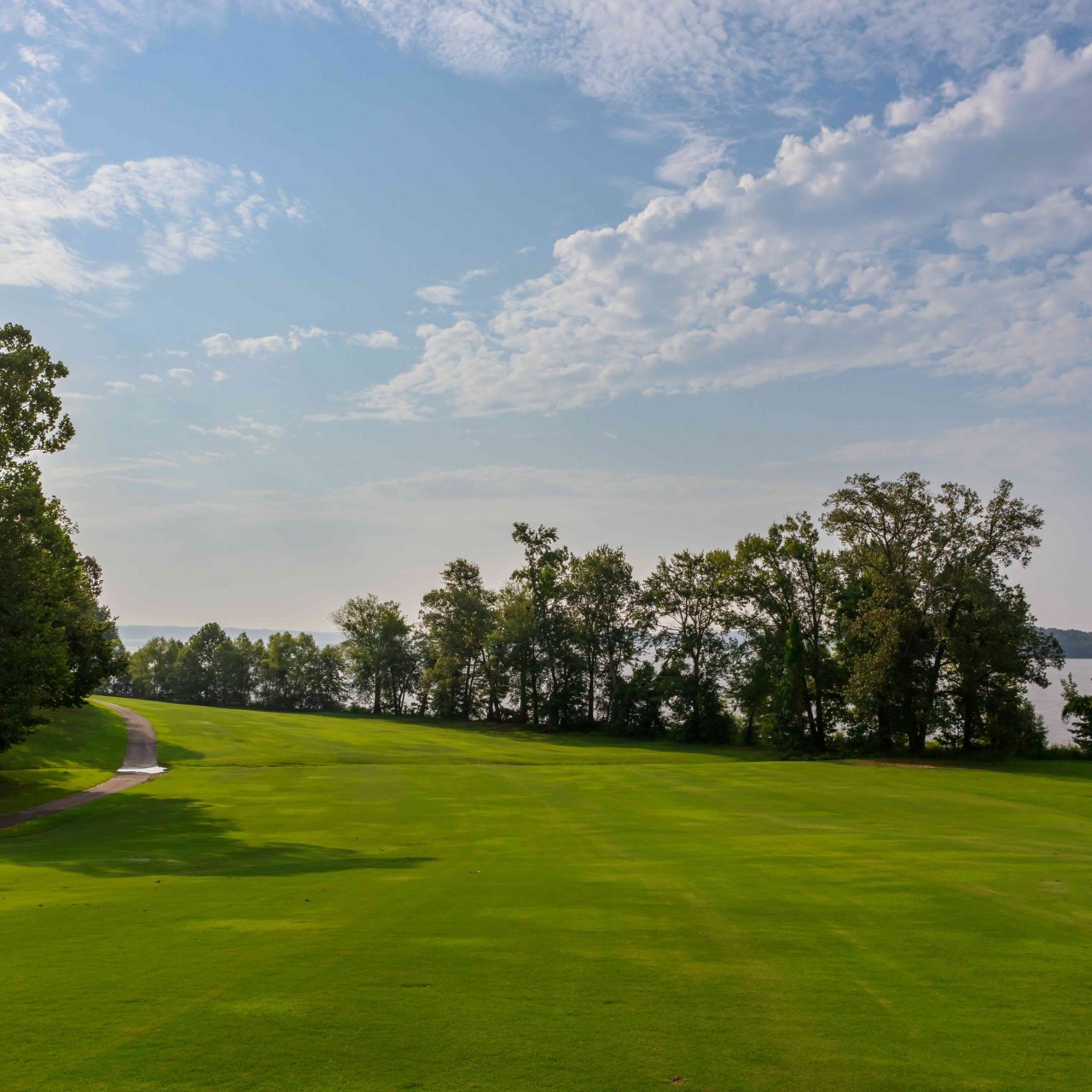 Lush golf course with a curving path near a lake under a clear sky.