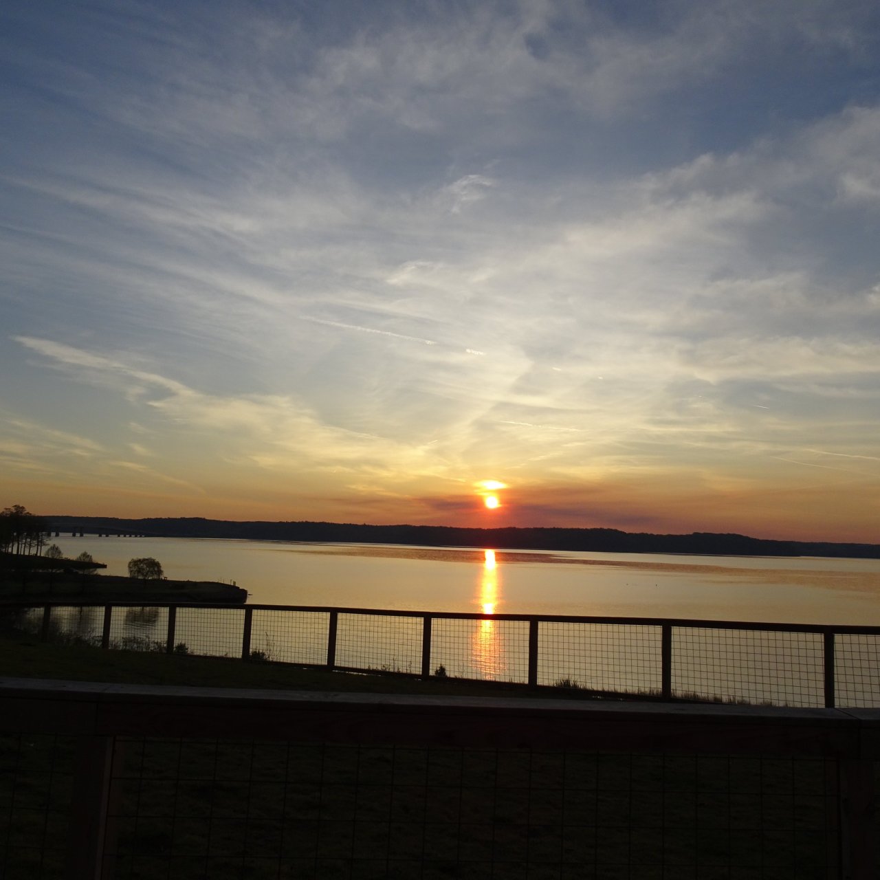 Sunrise over a calm lake with a silhouette of a guardrail in the foreground.