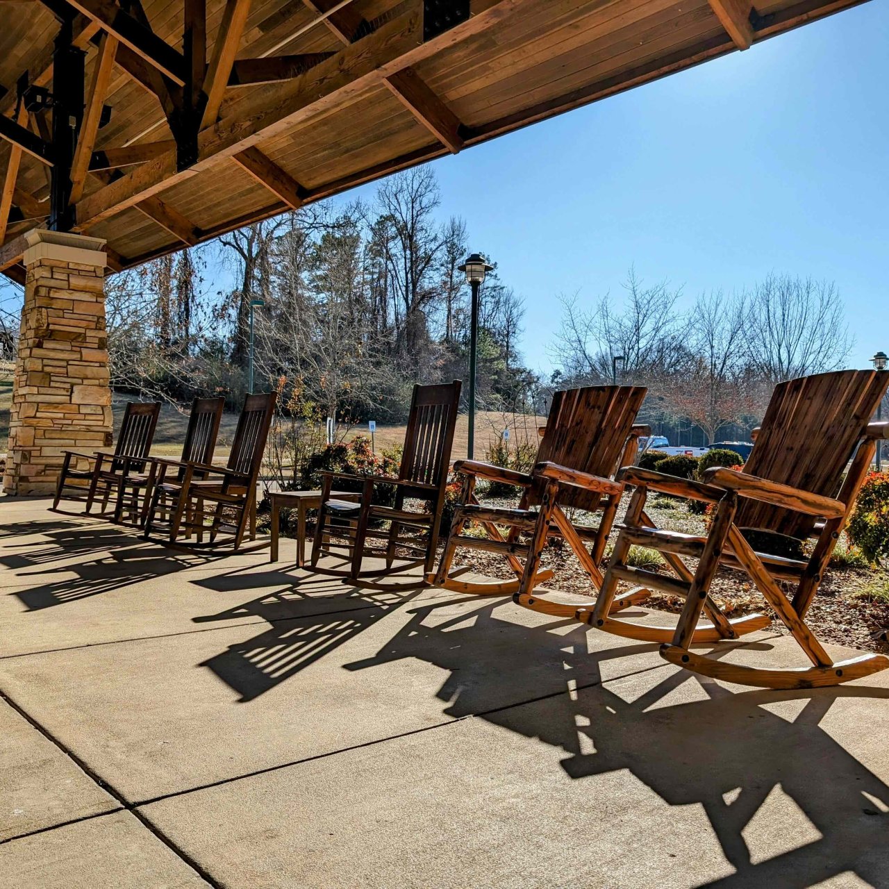 Several rocking chairs in a line under a covered entrance way.