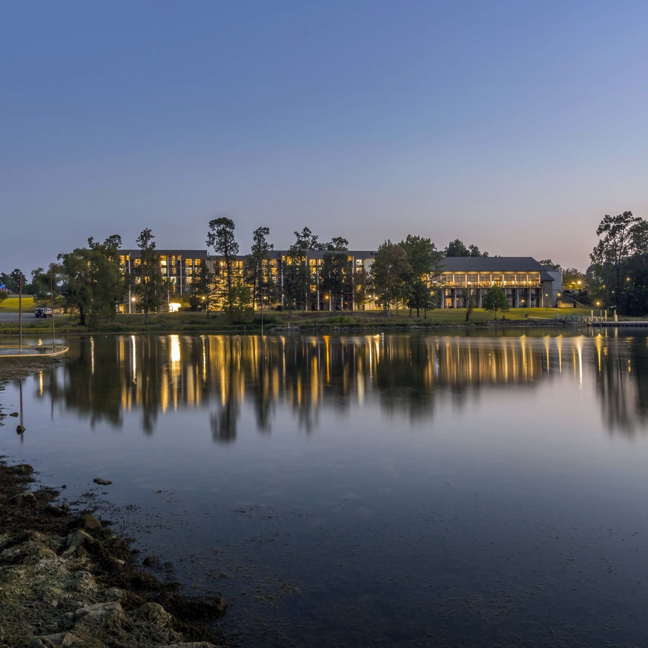 Twilight scene of a calm lake reflecting buildings and trees.