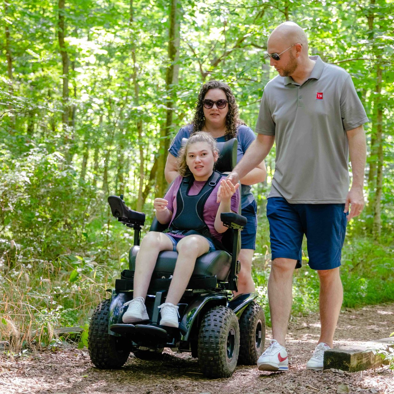 Family walking in the forest, child in a wheelchair smiling.
