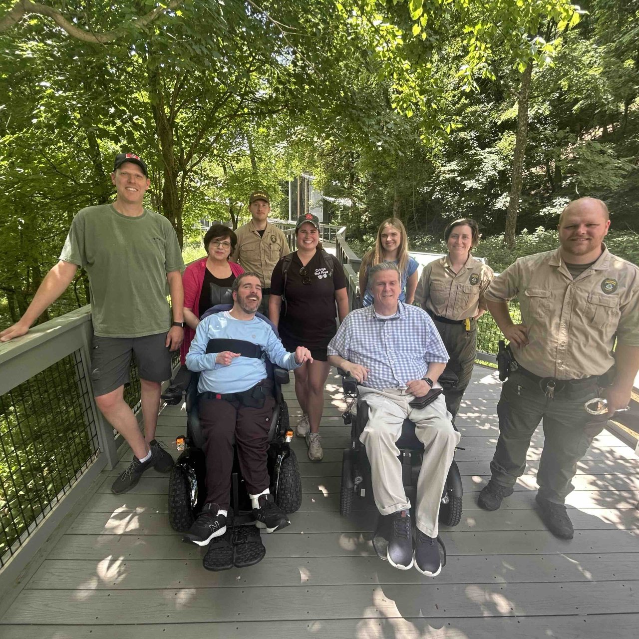 Group of eight people, some in wheelchairs, on a tree-lined pathway.