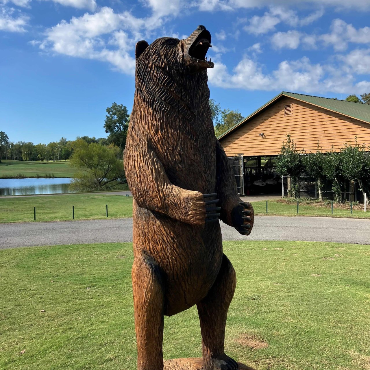 Wooden bear sculpture standing on a stump in front of a lake and building.