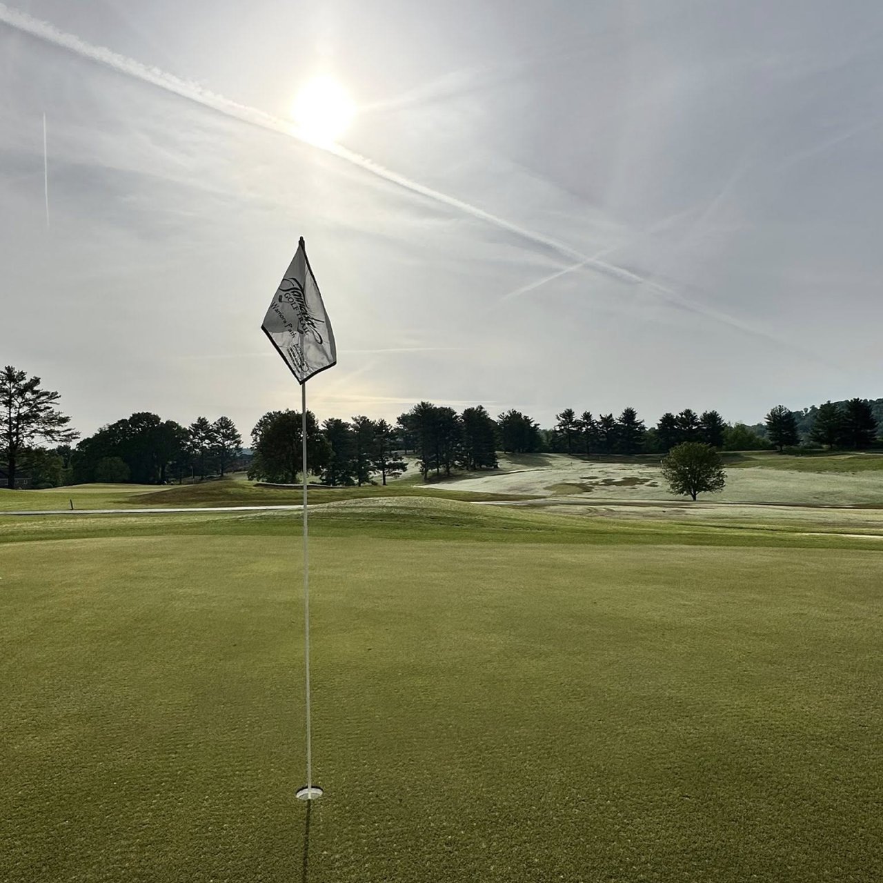 Morning sun over a golf course with a flagstick in the foreground.