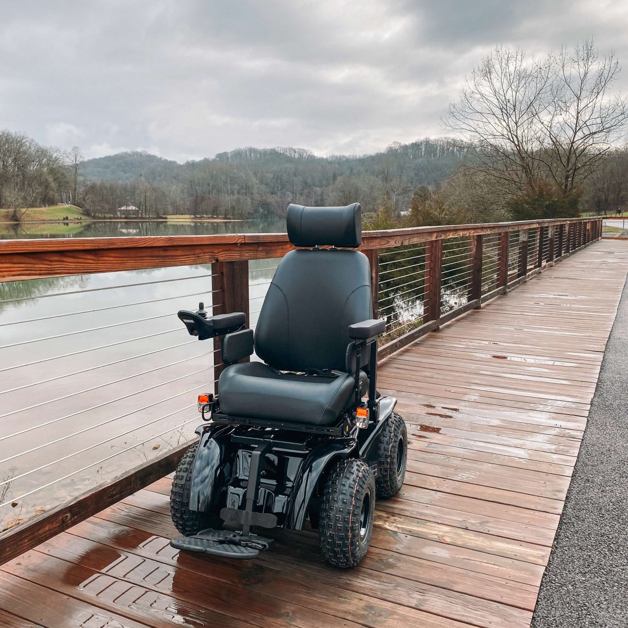 All terrain wheelchair on a bridge with wooden and wired railing.