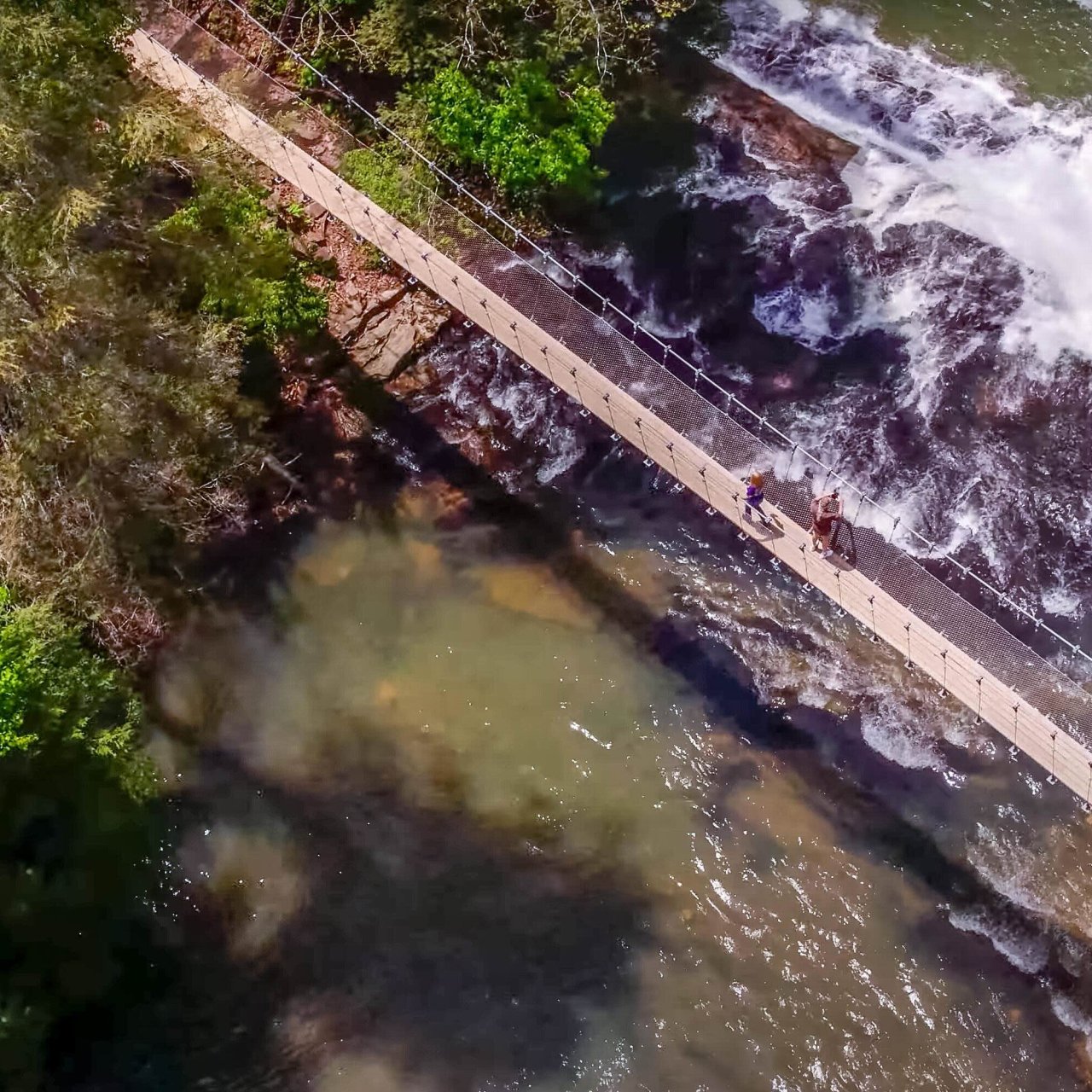 Aerial view of a thin bridge next to a waterfall.