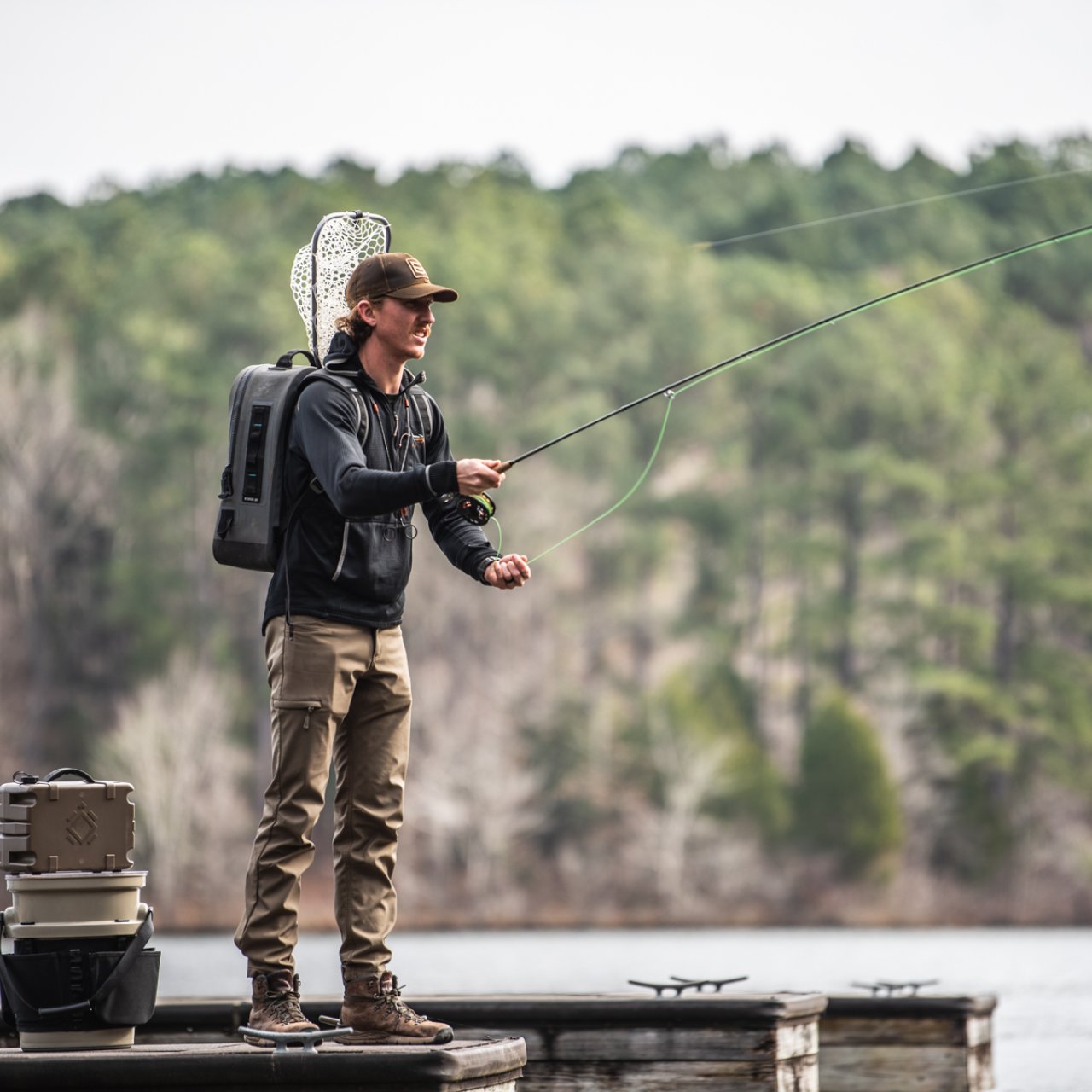 A man in fishing gear standing on a dock with a fishing line casted