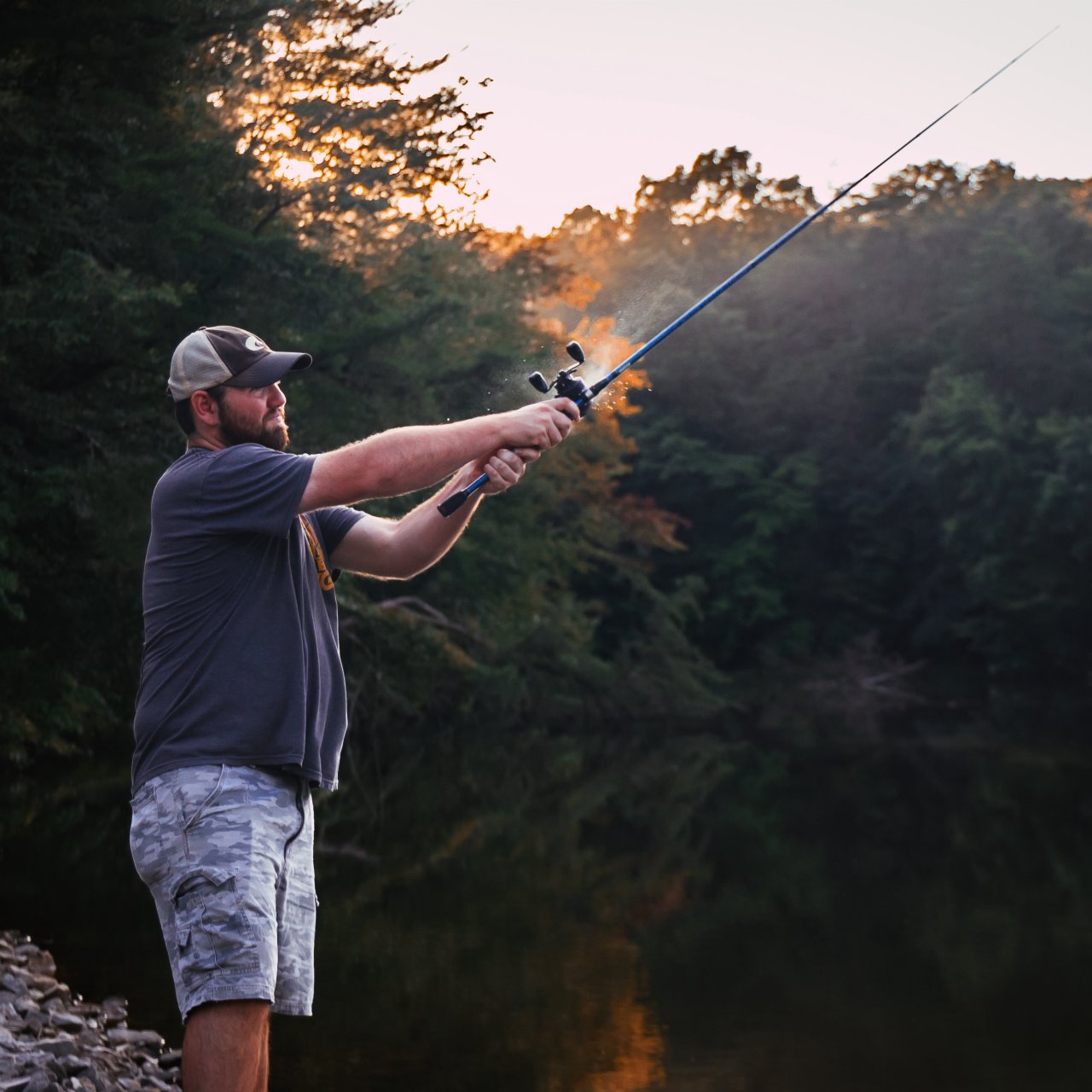 Man fishing by a serene river at dusk.