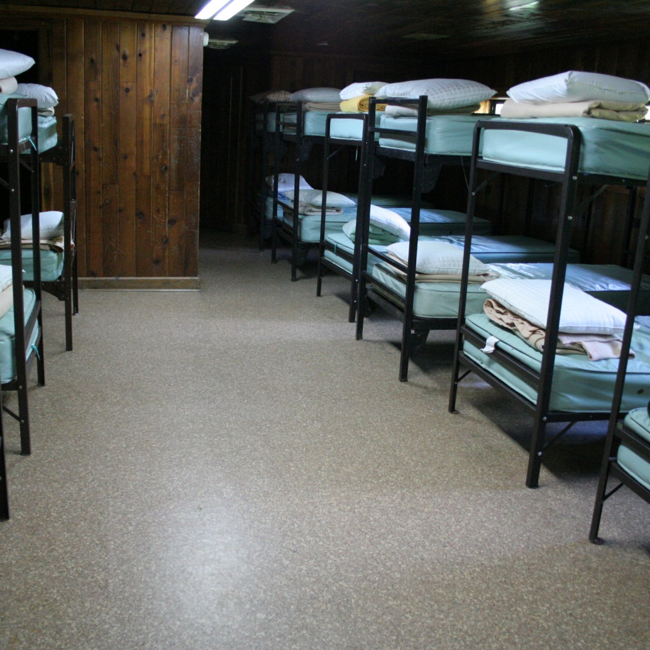Dormitory room with rows of bunk beds and wooden walls.
