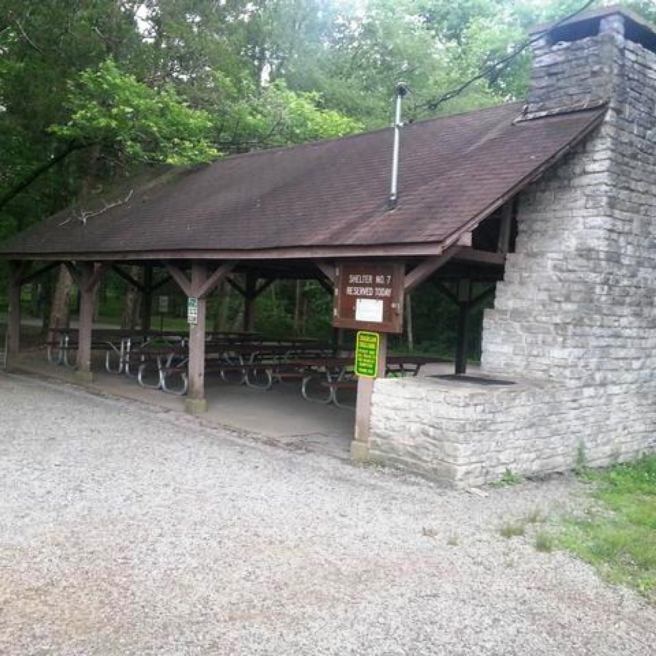 Shelter with stone chimney in a wooded area with picnic tables.