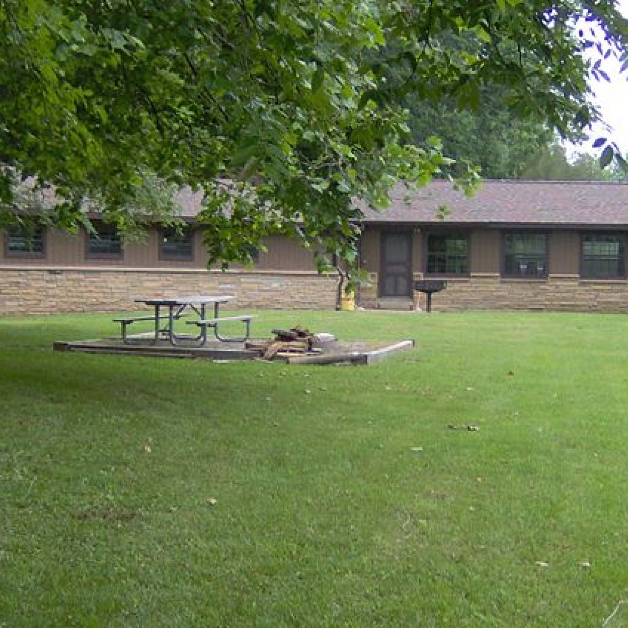 Brown house with a chimney, surrounded by trees and a grassy yard with a picnic table.