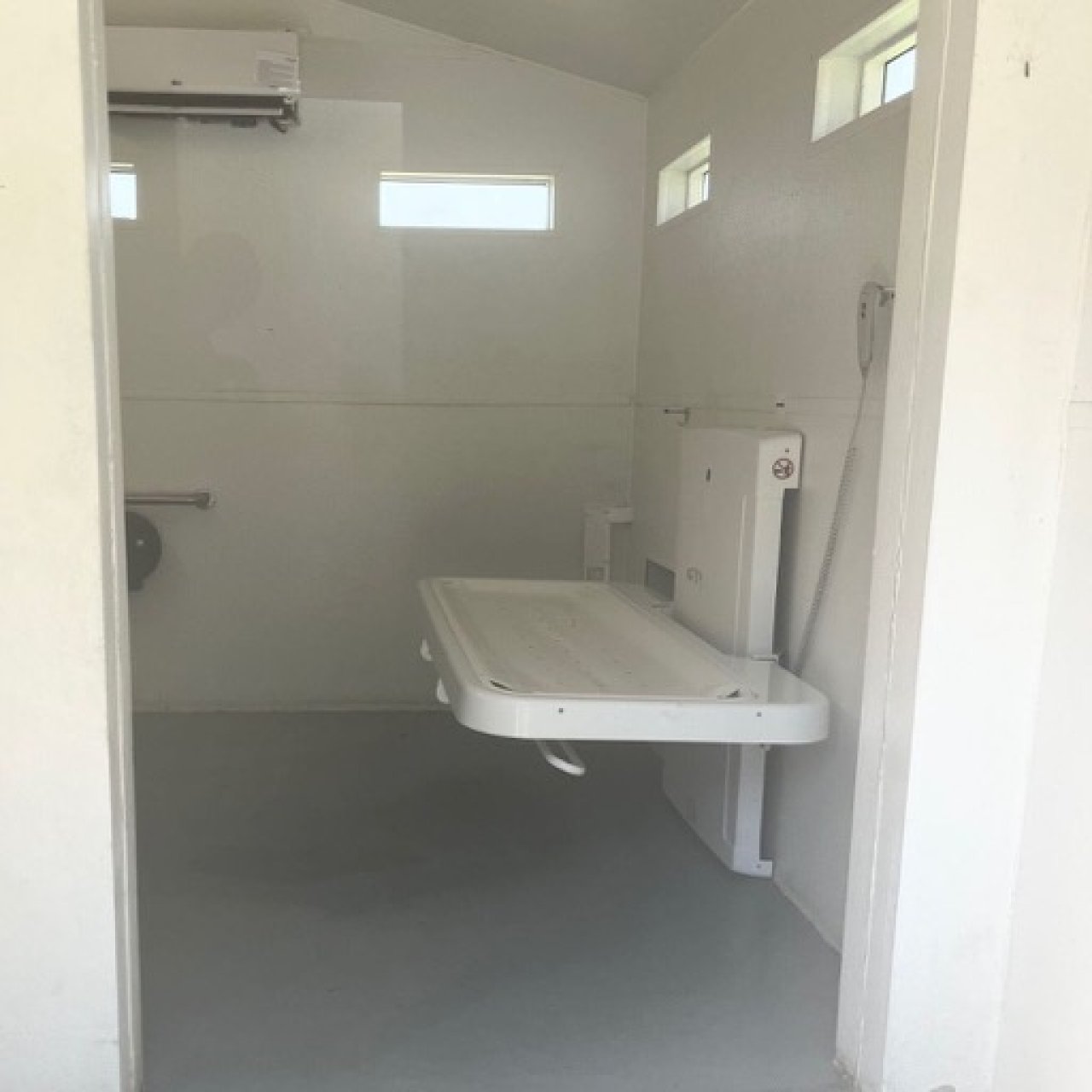 An adult-sized changing table is shown in the open position on the right hand side of a private restroom. 