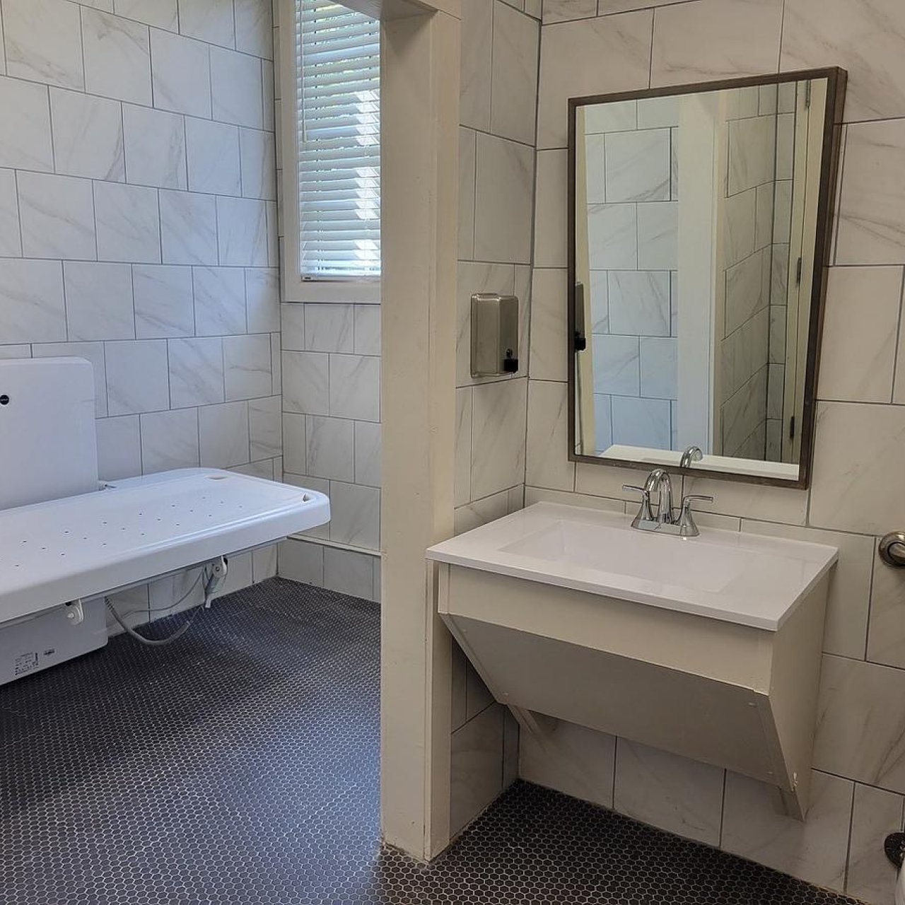 A private restroom with granite tiles has an adult-sized changing table to the left. On the right, a sink and toilet are available. 