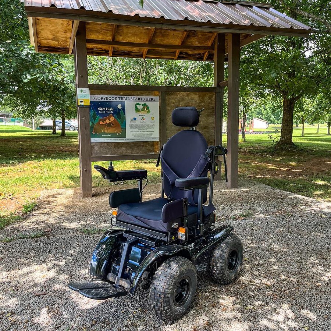 An all-terrain wheelchair sits on a paved surface at a trailhead.