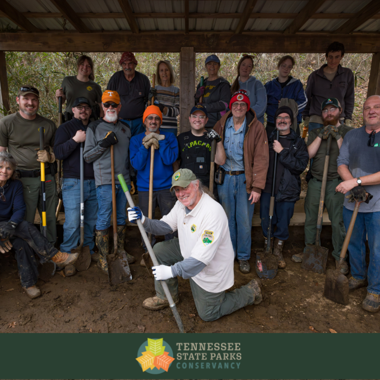 Volunteers standing and kneeling together outdoors, holding shovels and smiling after a conservation project.