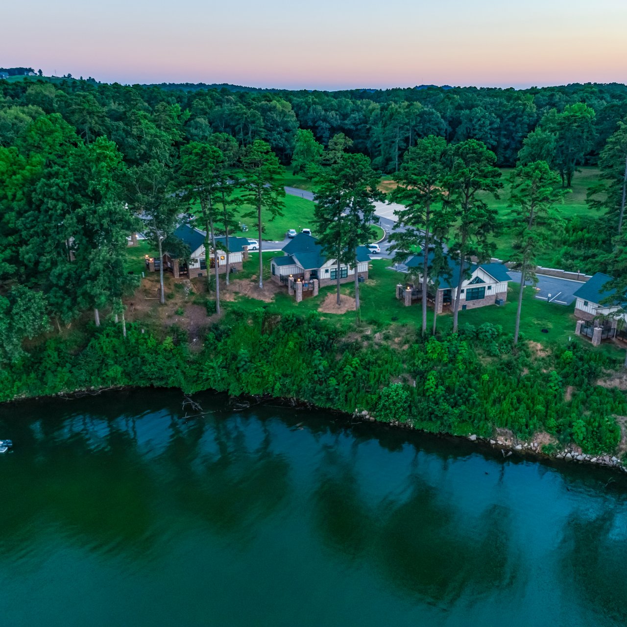Aerial view of a lakeside village surrounded by trees at sunset.