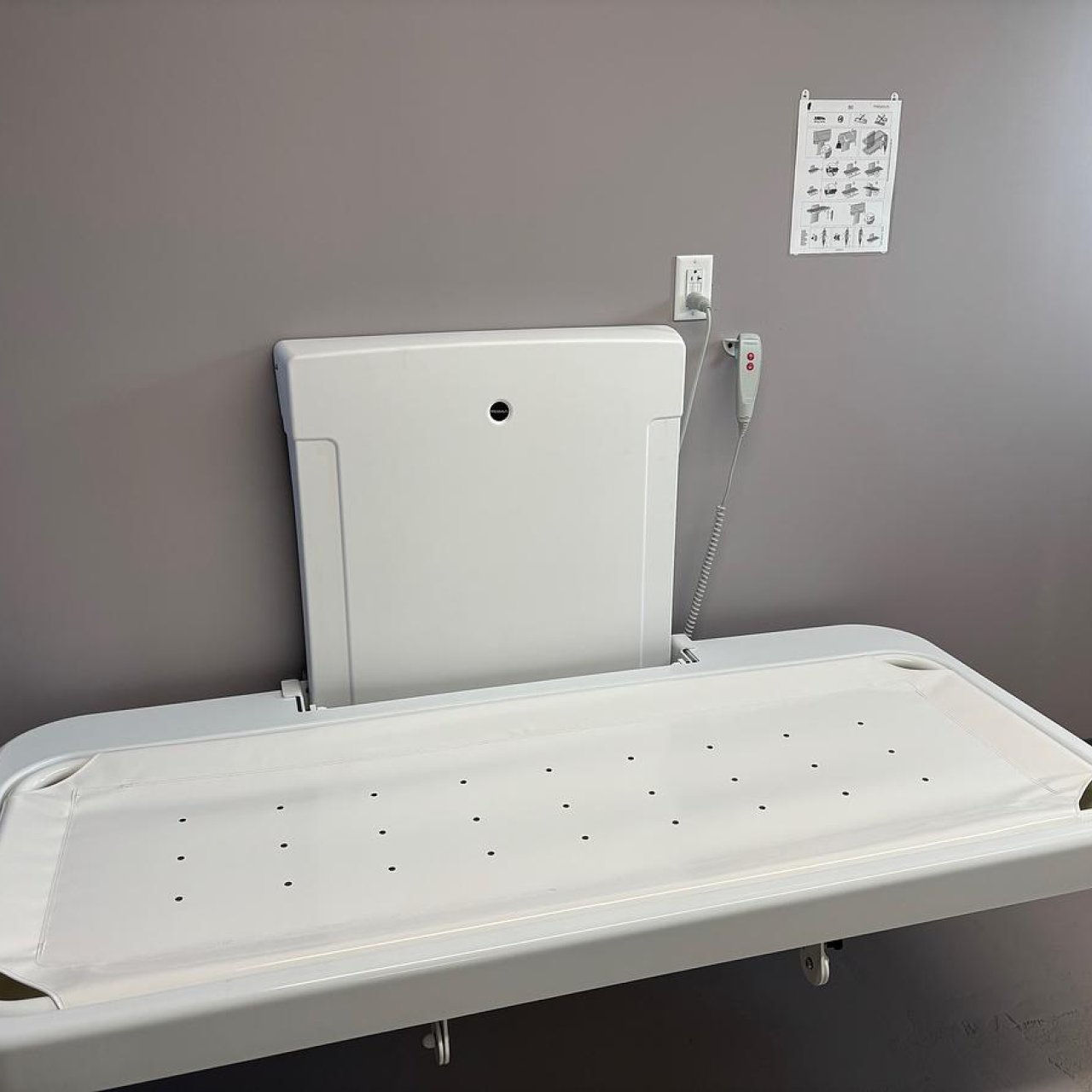 Wall-mounted adult-sized changing table in a gray room.