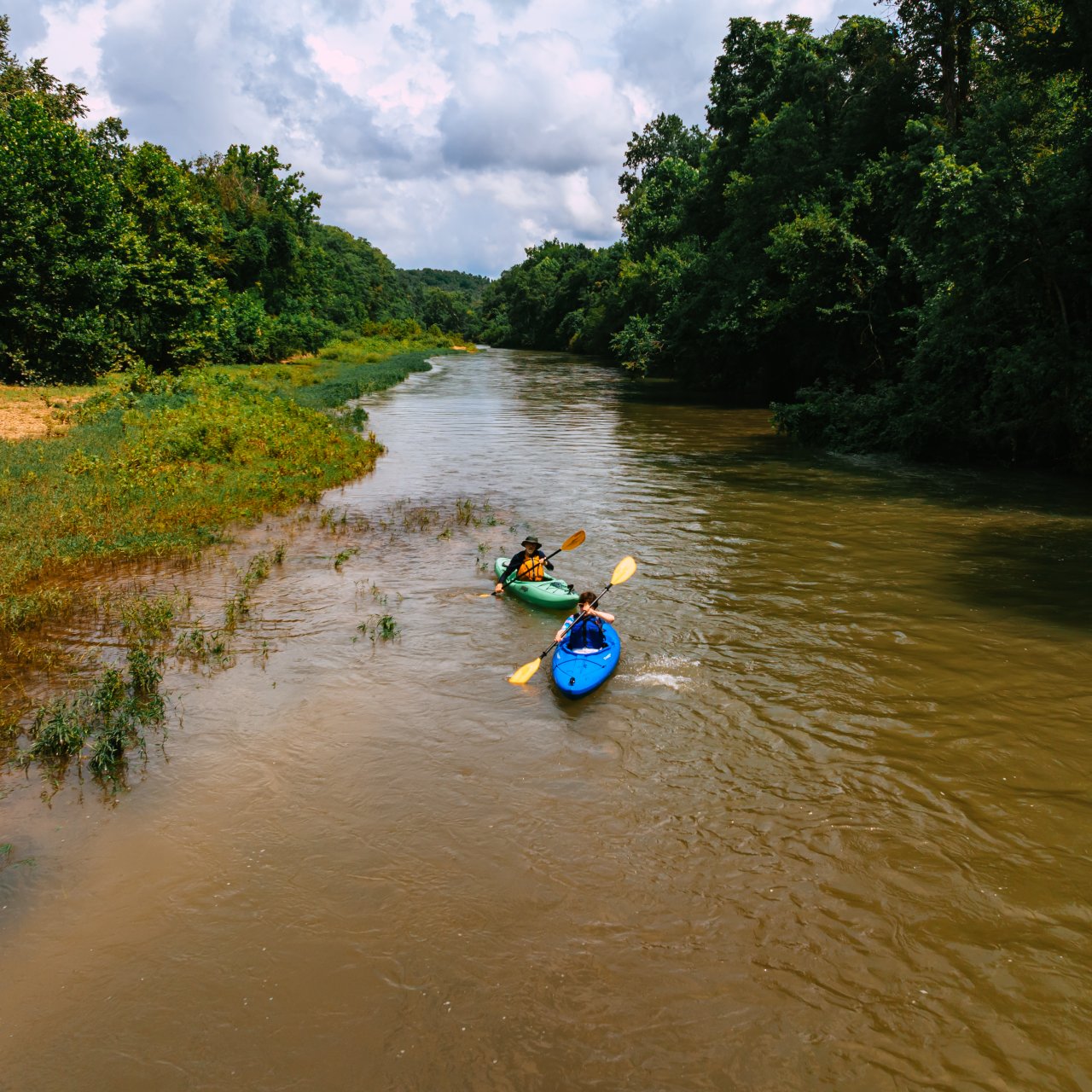 Two kayakers paddling down the Buffalo River river surrounded by lush greenery.